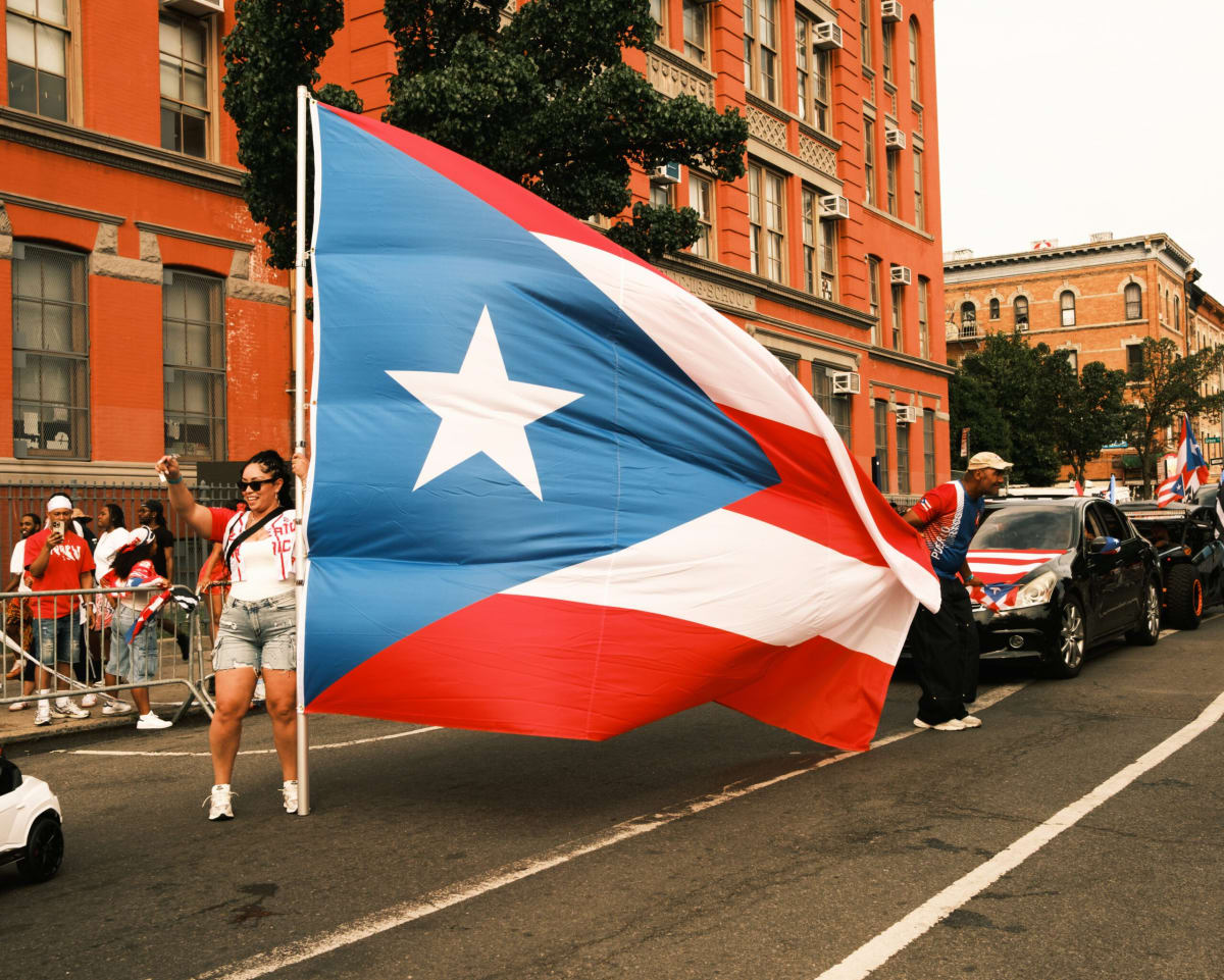 Families celebrate at Bushwick Puerto Rican Day Parade with red white blue flags
