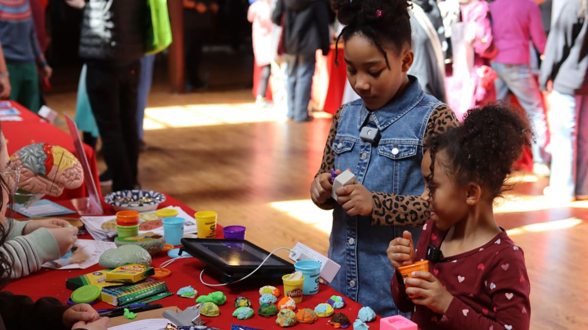 Young boy and father demonstrate brain's electrical signals causing involuntary finger movements at Brown Brain Fair
