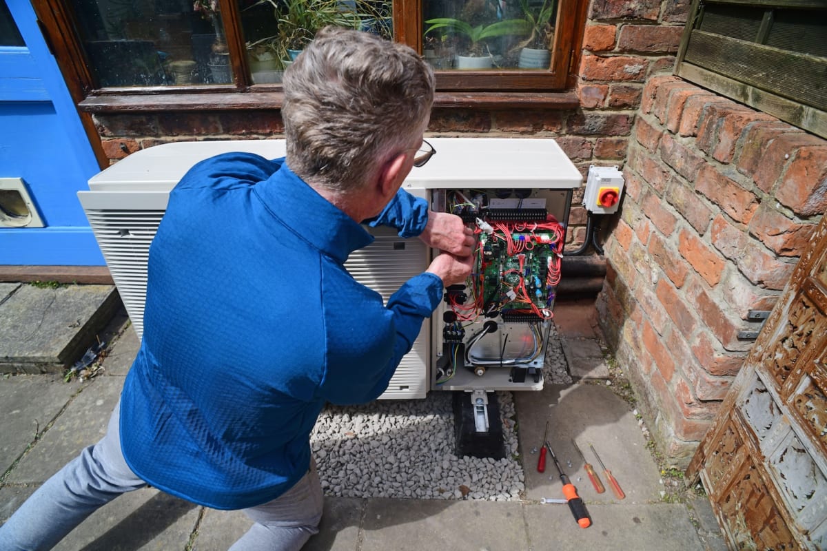 ** Engineer installing modern heat pump system on exterior wall of UK home