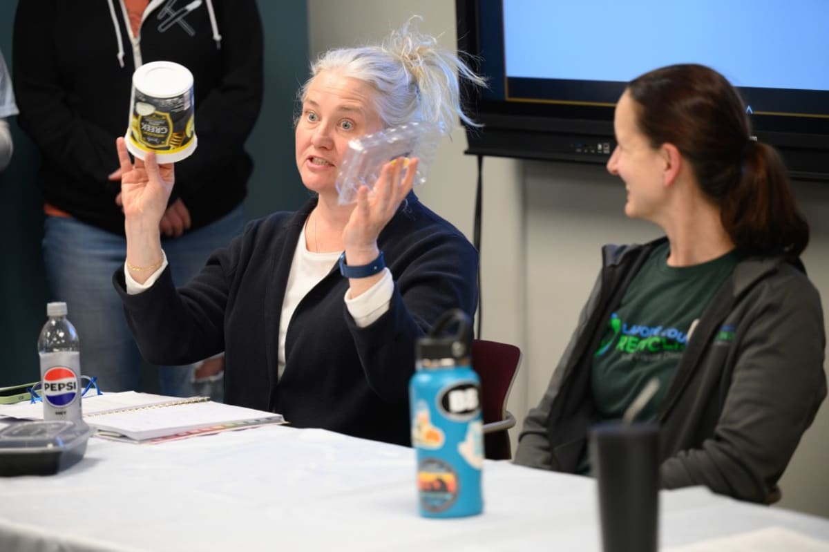 ** Environmental educators holding recyclable containers during interactive game show style recycling education event