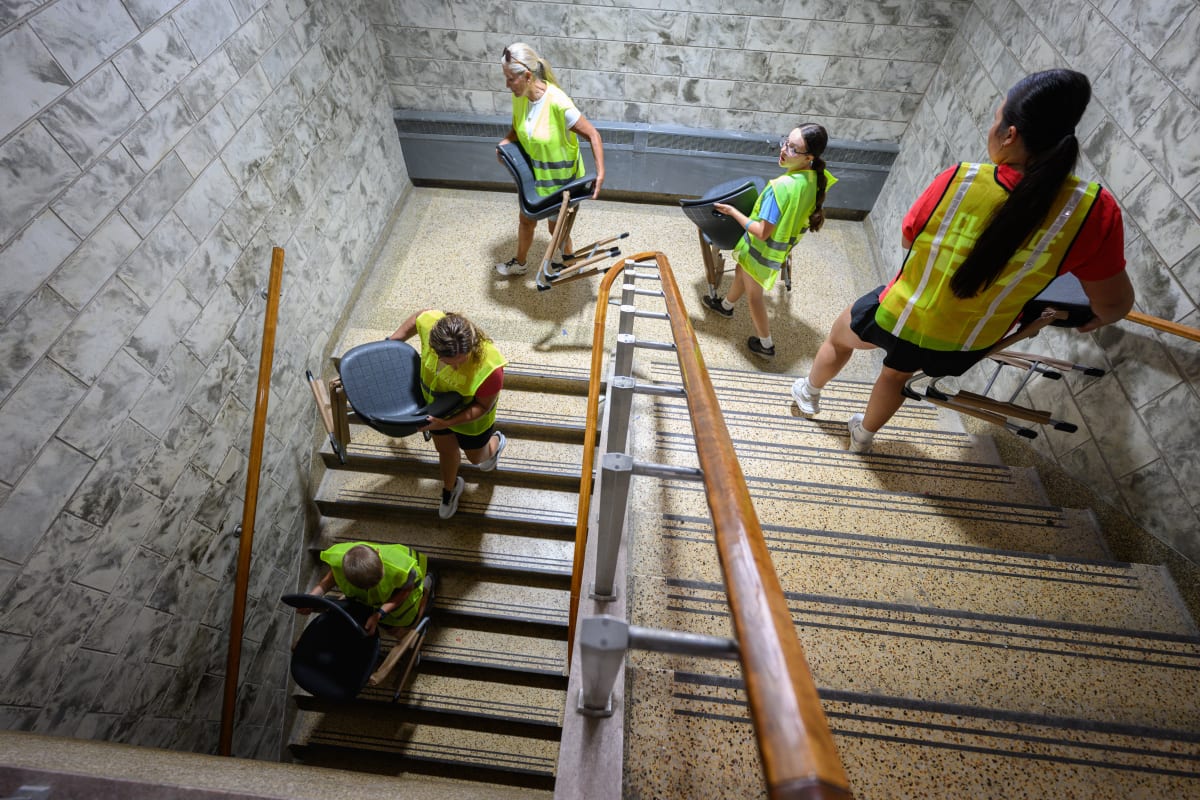 Volunteers in neon green vests carry chairs and furniture through Andrean High School hallways