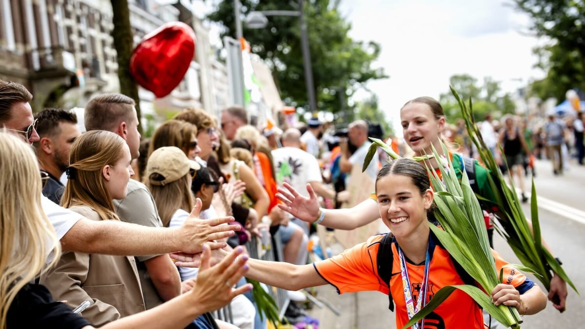 Thousands of walkers crossing finish line holding gladioli flowers at Nijmegen march