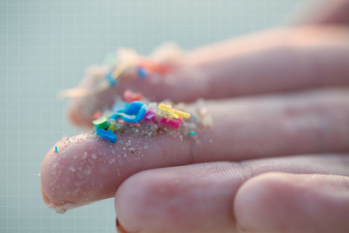 Close-up of fingers holding tiny plastic debris pieces representing microplastics pollution