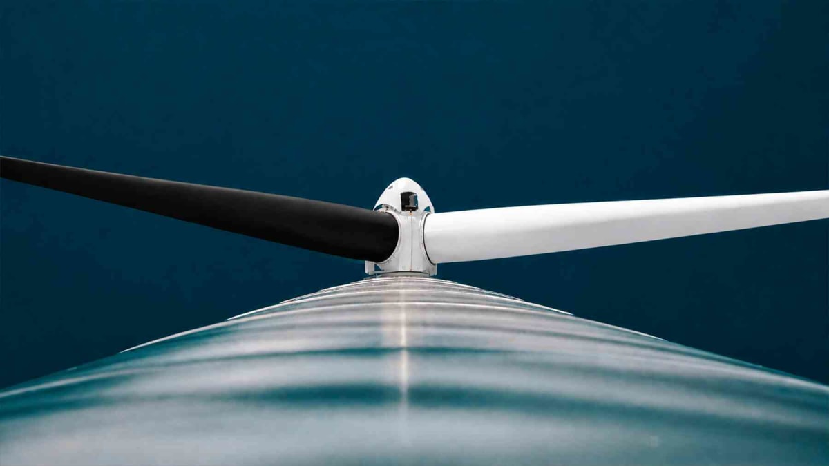 Wind turbine with one black blade and two white blades spinning against blue sky