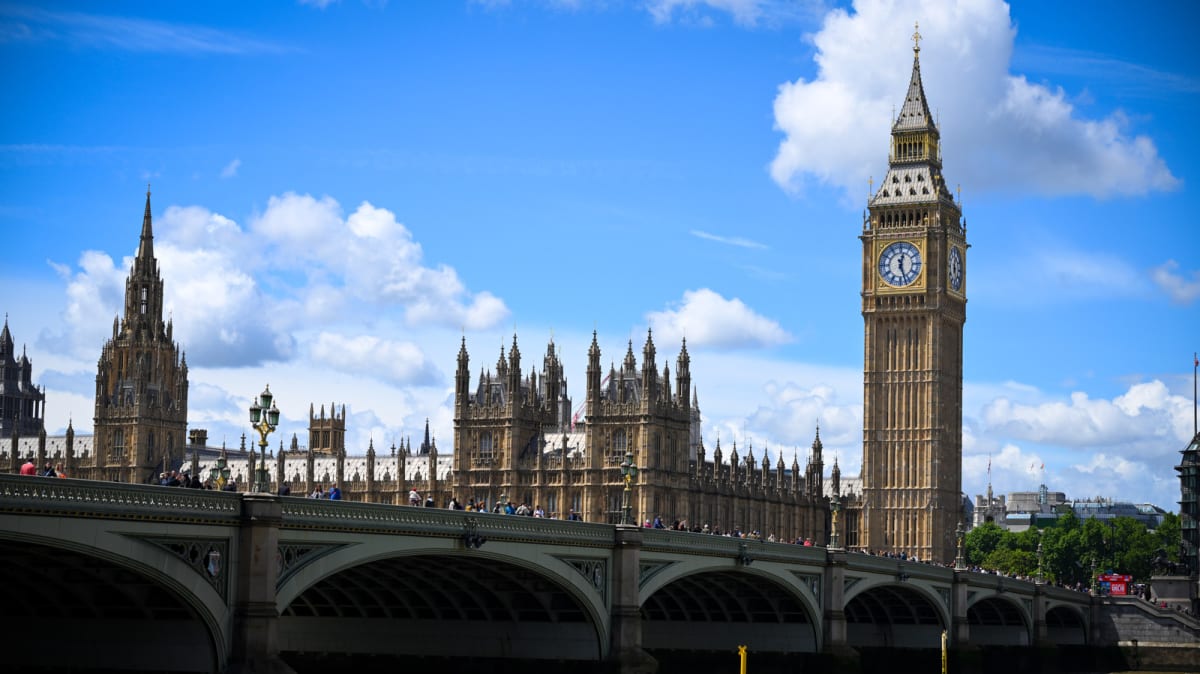 Yellow Playdate handheld gaming device with hand crank being used at Big Ben clock tower