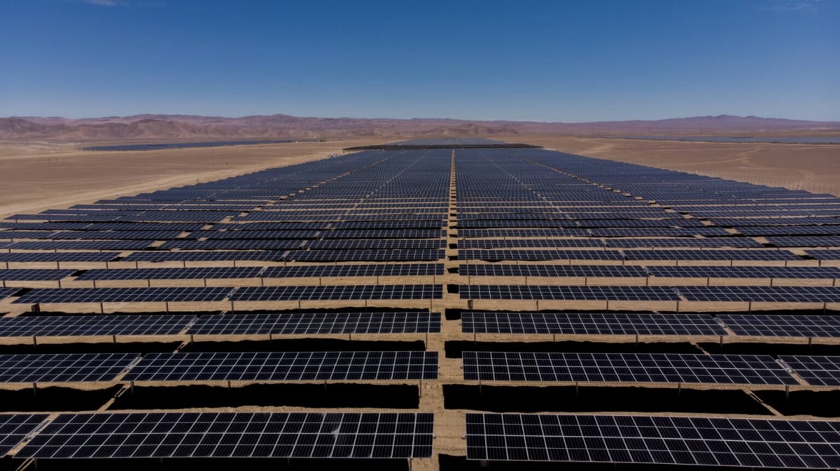Expansive solar panel arrays stretching across Chile's sunlit Atacama Desert landscape with battery storage facilities