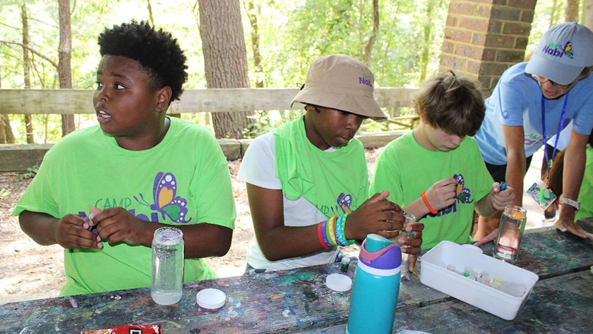 Children participating in outdoor summer camp activities with adult volunteers and therapy dogs