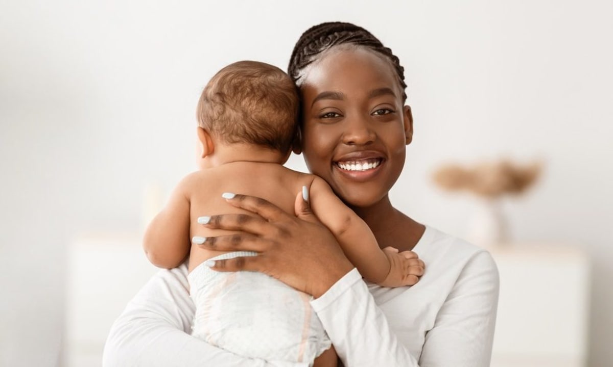 Black mother holding baby while video chatting with therapist on laptop at home