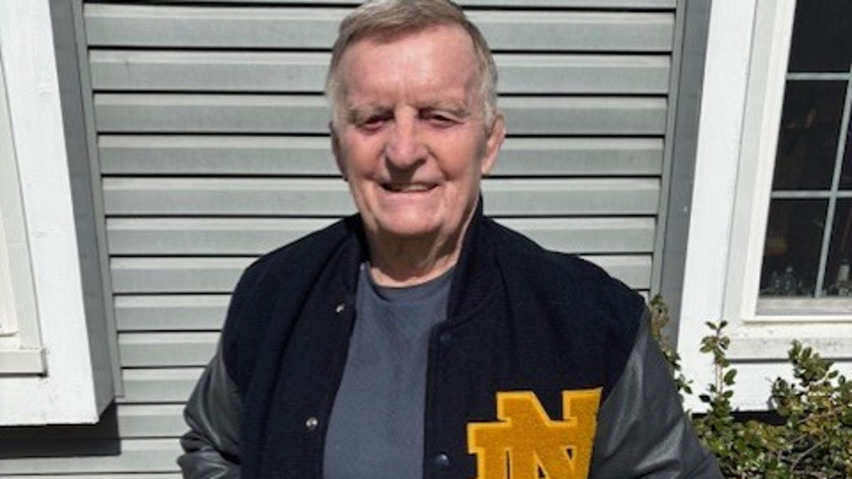 ** Fran McCann, 85-year-old wrestling coach, standing in gym wearing coaching attire