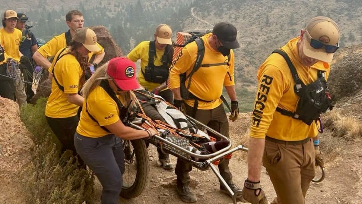 Search and rescue volunteers carrying wheeled litter on mountain trail in central Oregon