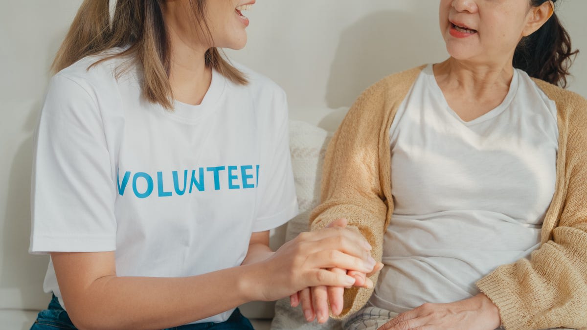 Volunteer holding elderly hospice patient's hand in comfortable home setting, showing compassion and connection
