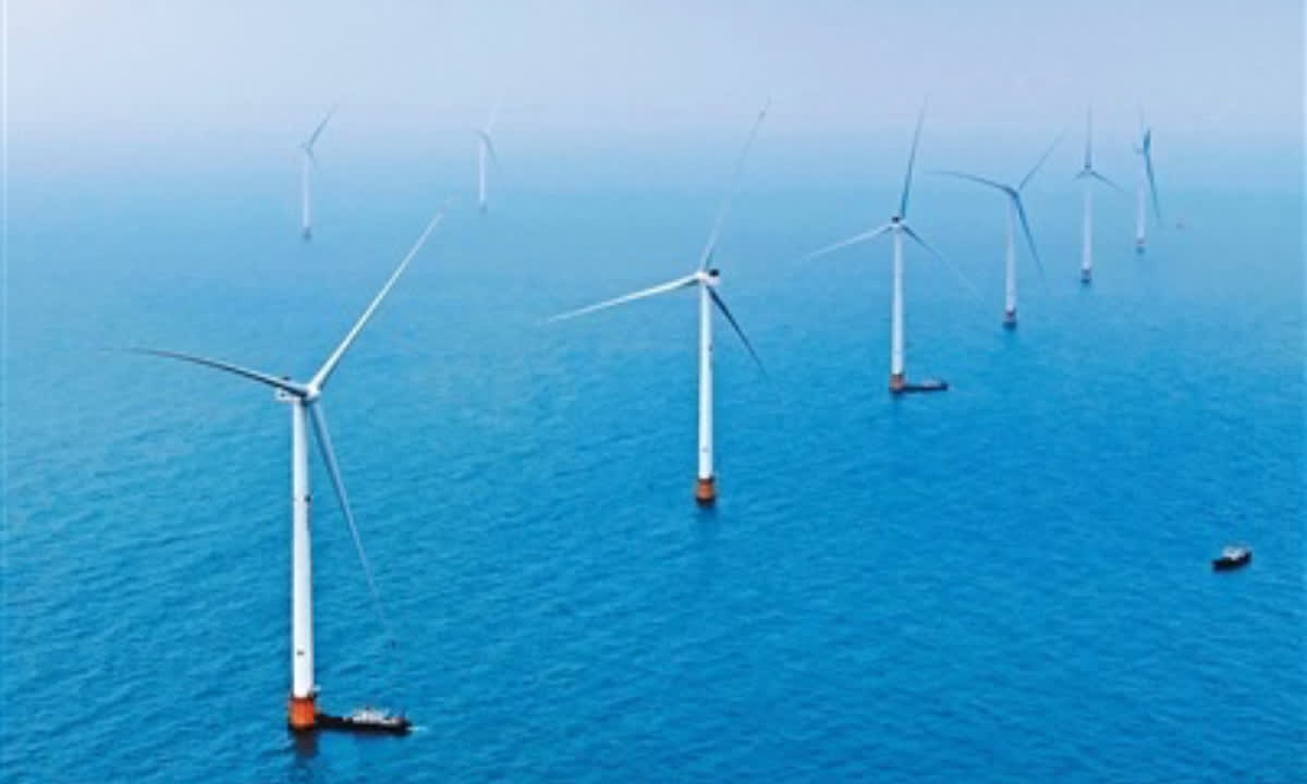 ** Massive offshore wind turbines with long white blades spinning above ocean waters in Hainan Province