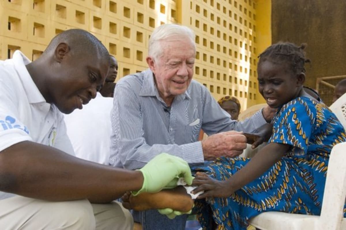 Health worker educating community members about Guinea worm disease prevention in rural village setting