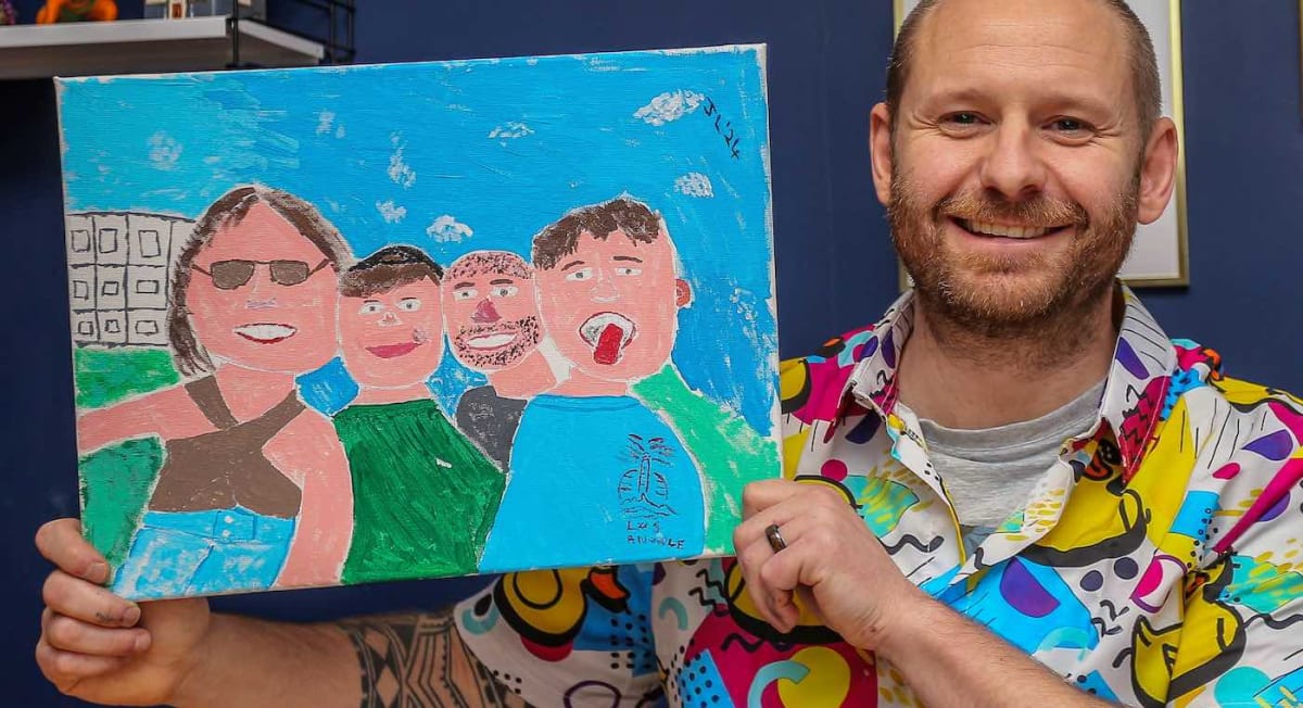 Jamie Lee Matthias holding a colorful, intentionally imperfect family portrait painting in his art style