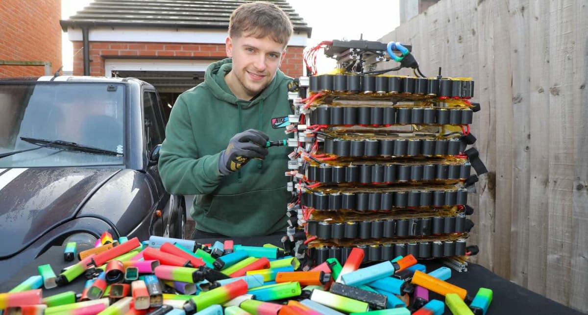Young engineer Chris Doel standing next to small electric G-Wiz car powered by recycled vape batteries