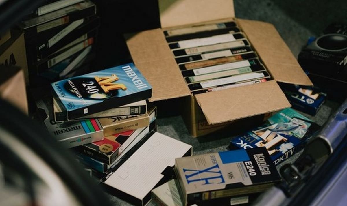 Person's hands holding stack of old VHS tapes and photo albums for digitization