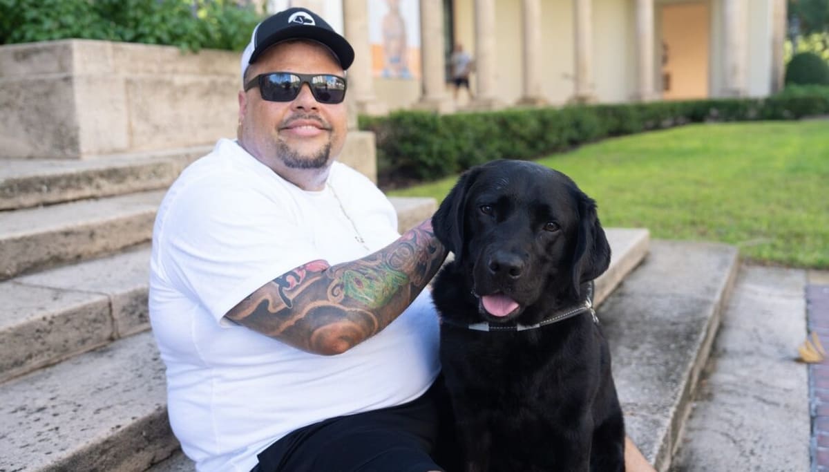Luis Perez sitting with his black Labrador guide dog Jerry who saved his life