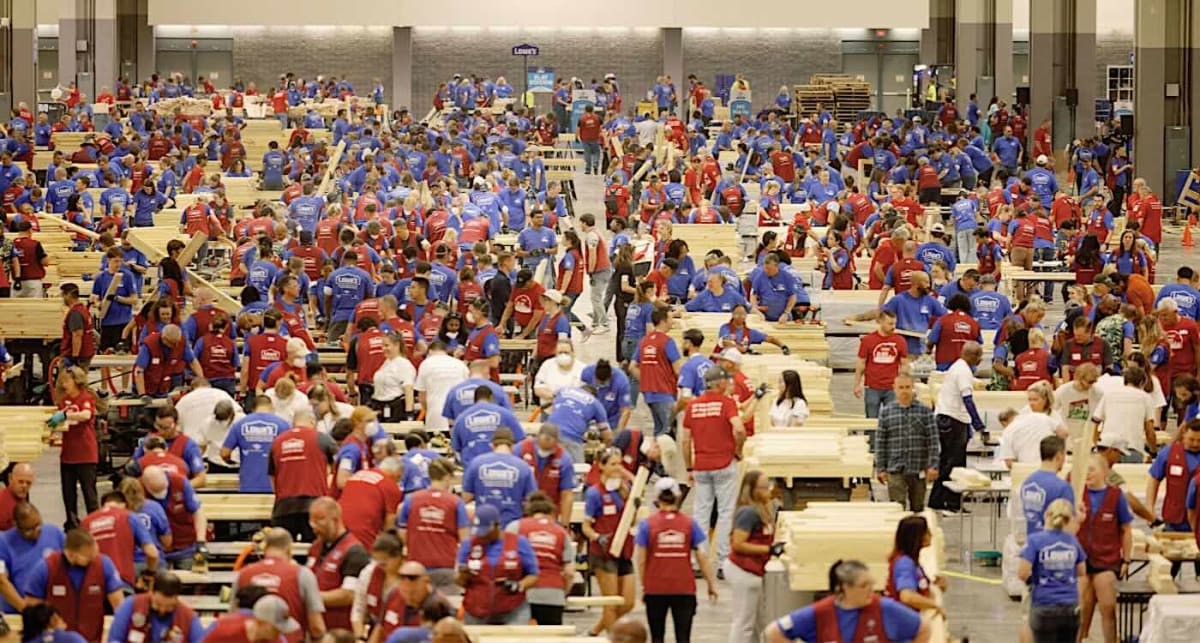 Volunteers assembling wooden beds in long assembly lines inside Charlotte Convention Center