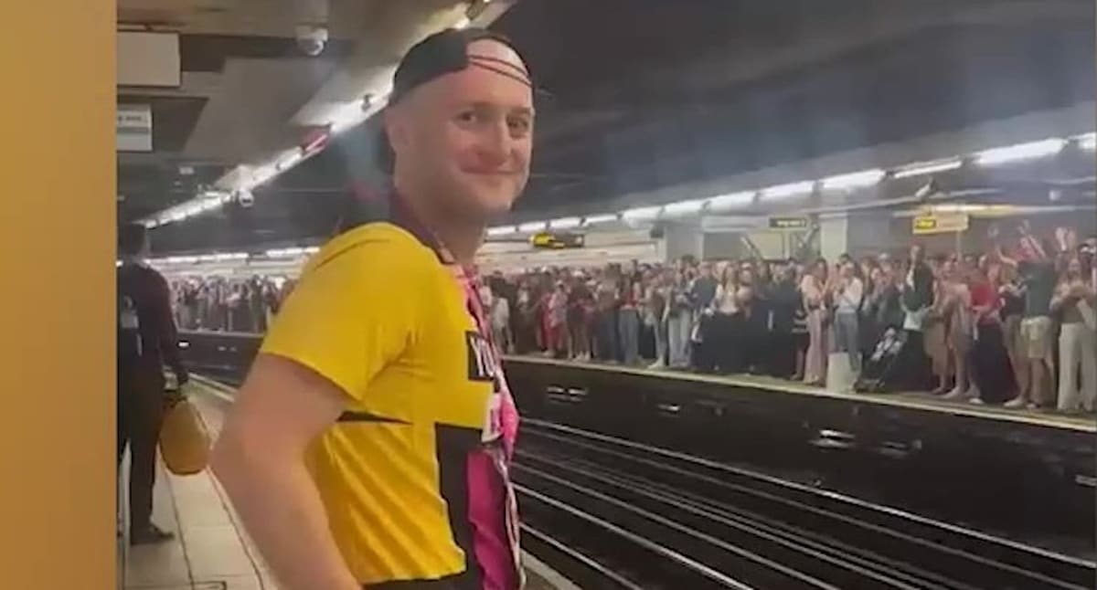 Marathon runner in medal stands on subway train as crowd applauds from platform