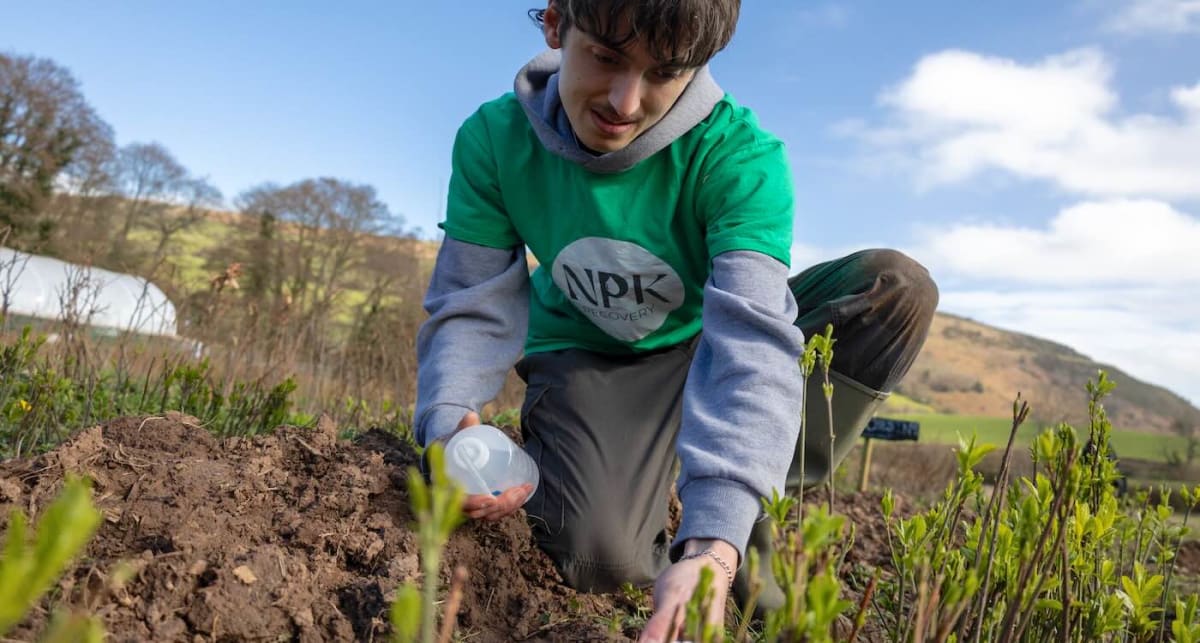 Young scientist in field applying sustainable fertilizer to soil for tree planting project