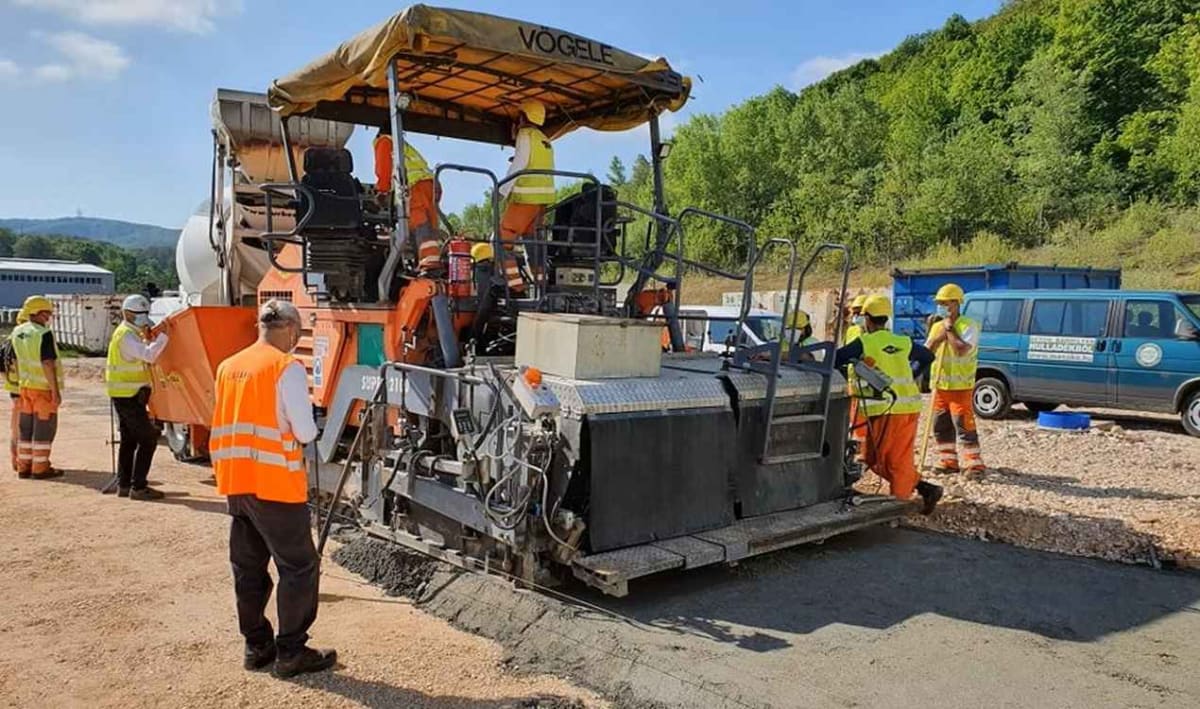 Workers pouring gray Waste Light Concrete mixture containing shredded recycled materials onto road surface