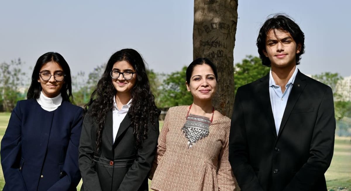 Three Indian teenage students holding their Plas-Stick invention with their teacher at award ceremony