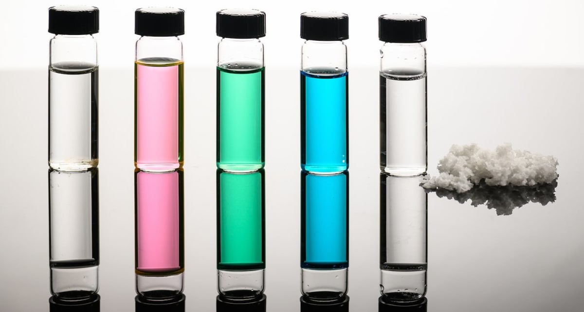 Five vials showing progression from seawater to clear desalinated water with recovered salts beside them