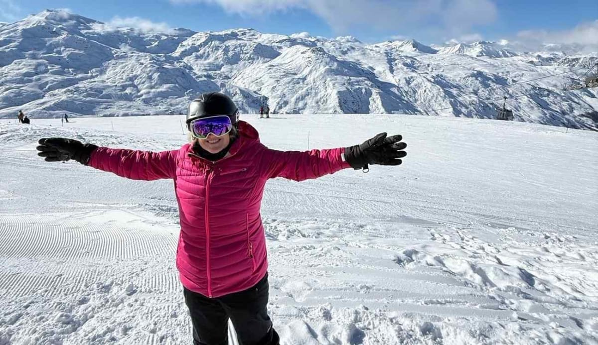 Smiling woman in winter gear stands on snowy Alpine mountain slope after lupus remission