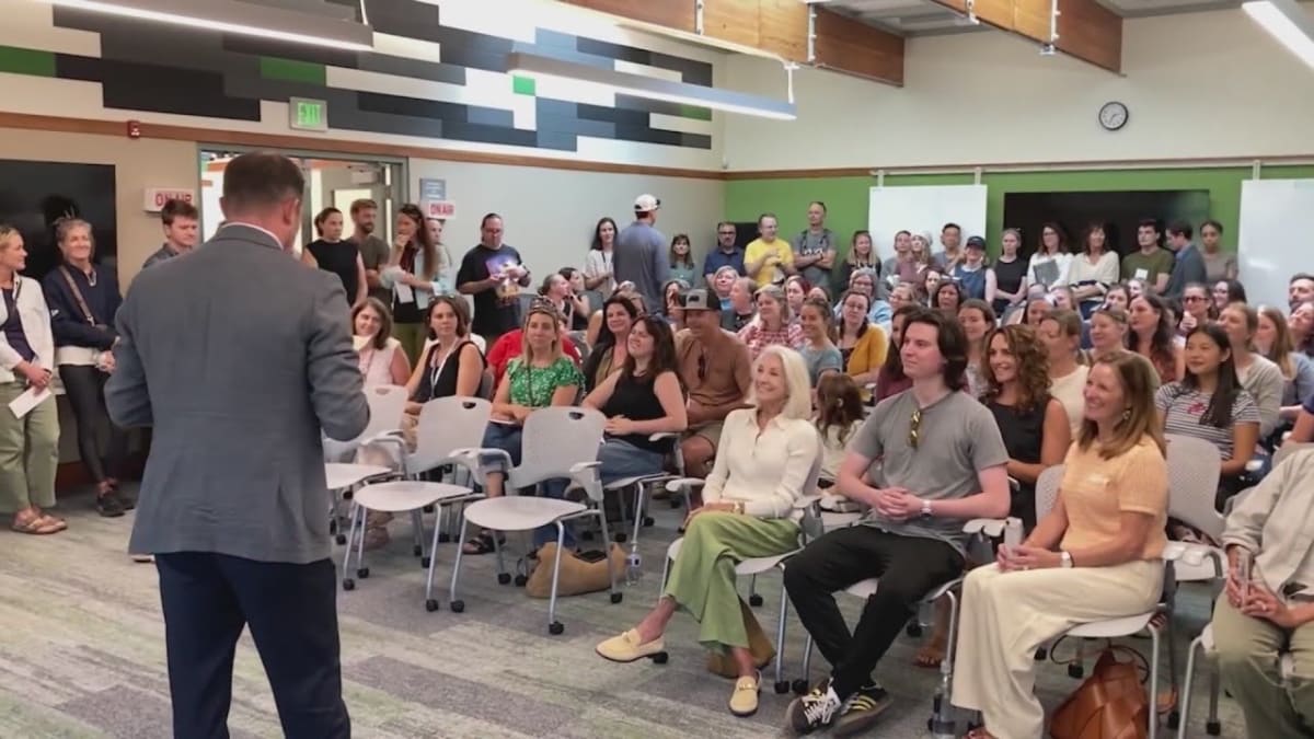 Teachers in conference room holding checks and reacting emotionally to surprise bonuses from donor