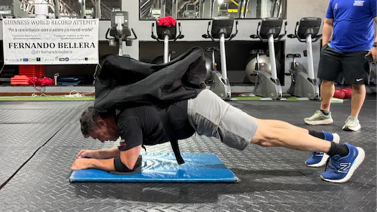 Venezuelan neurosurgeon Fernando Bellera performing weighted plank exercise with heavy pack on back