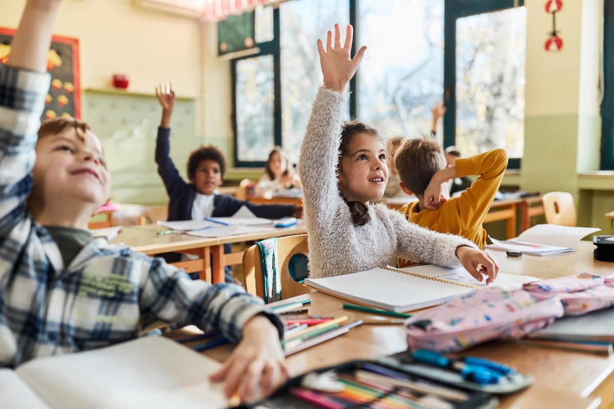 Diverse elementary students raising hands eagerly in bright Florida classroom with smiling teacher