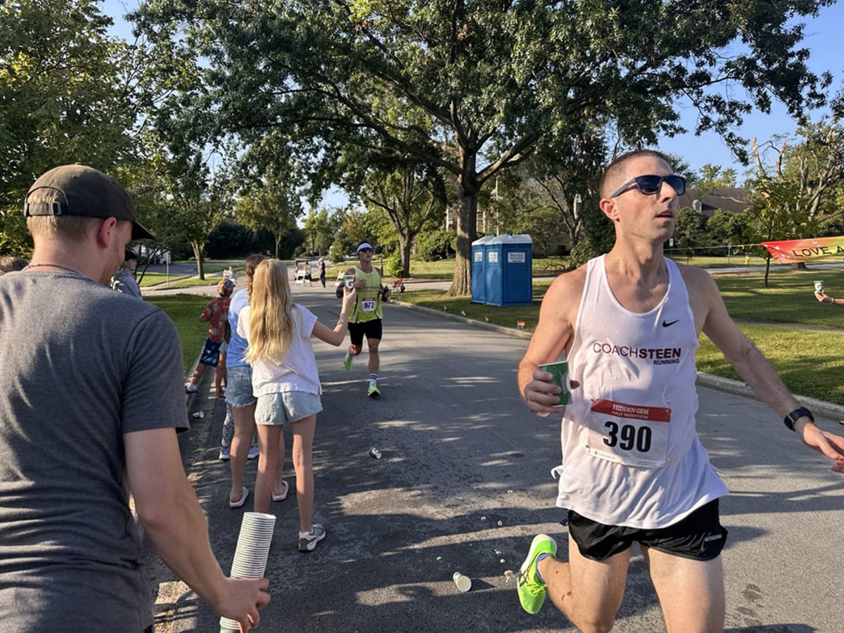 Volunteers hand water cups to half marathon runners on decorated neighborhood street