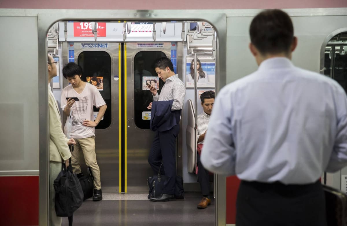 Japanese person holding smartphone with multiple carrier signal bars displayed during emergency
