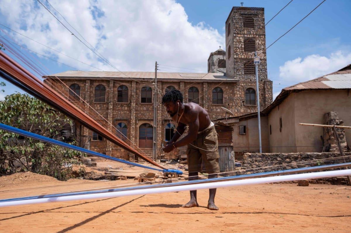 Nigerian artisan working on traditional handloom weaving colorful aso-oke fabric in outdoor workshop