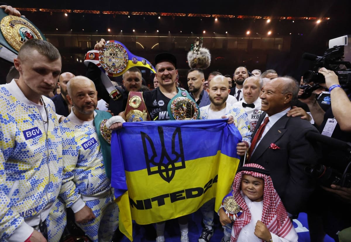 Ukrainian boxer Oleksandr Usyk holding championship belts and displaying Ukrainian symbols after victory