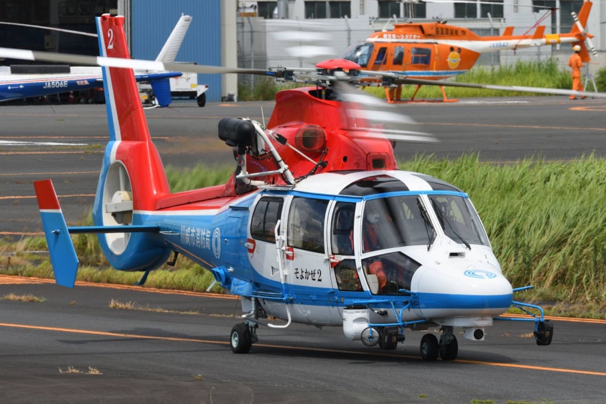Red and white emergency helicopter flying over Japanese landscape during rescue mission