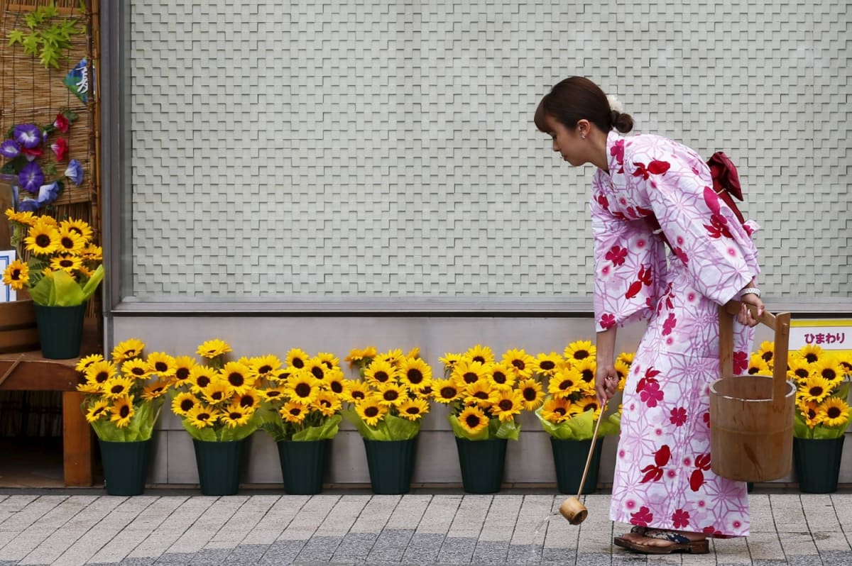 Japanese shopkeeper pours bucket of water onto hot pavement outside store entrance in summer