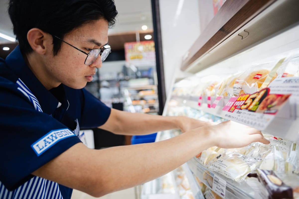 Foreign worker serving customer with a smile at Japanese convenience store counter