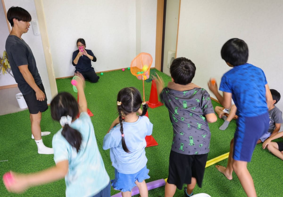 Children playing with colorful balance balls in bright Japanese community center classroom