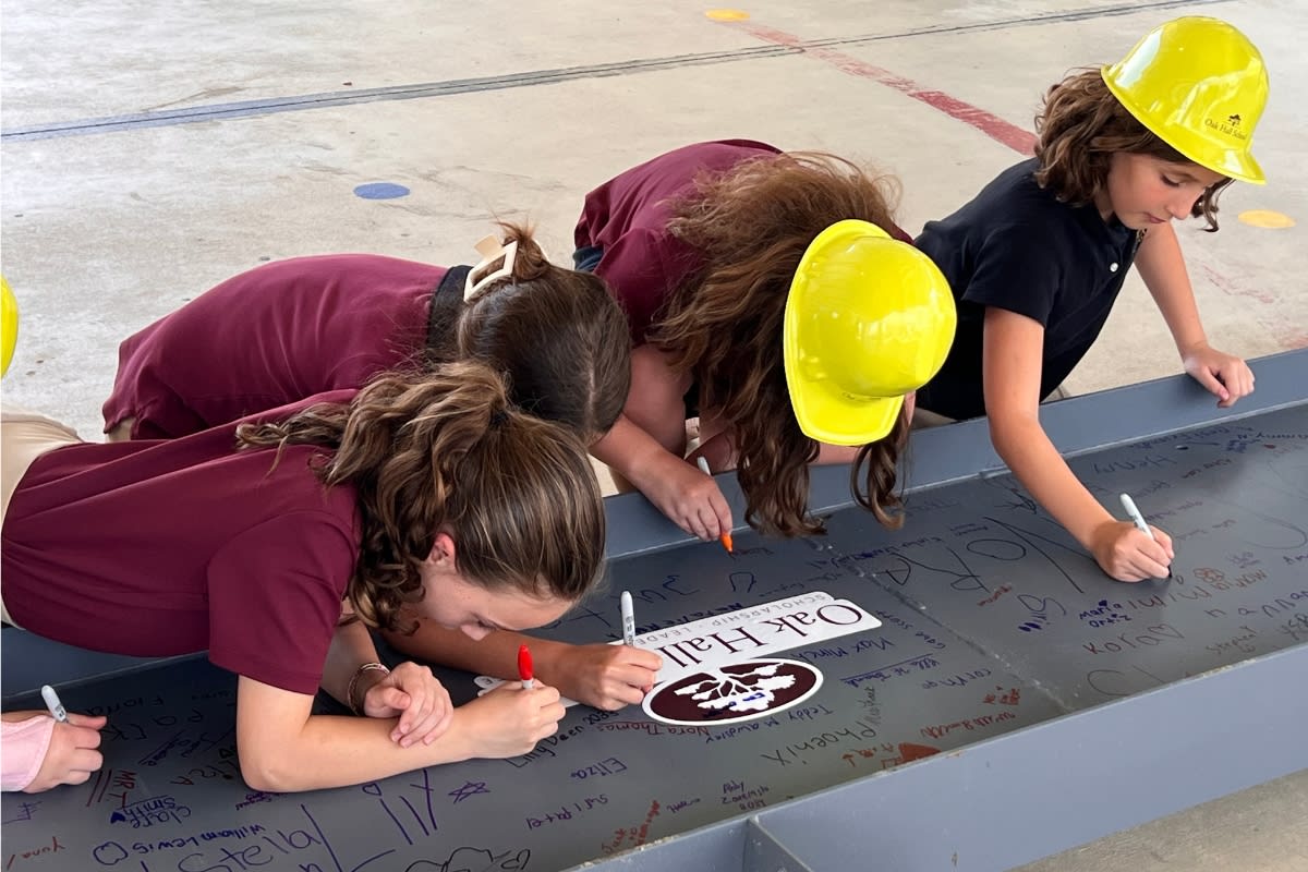 Oak Hall School students wearing hard hats sign steel beam with markers for new gymnasium construction