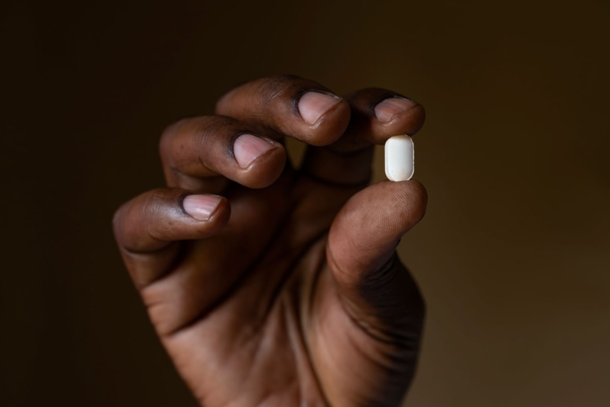 Healthcare worker administering oral medication tablets to patient in rural African clinic setting