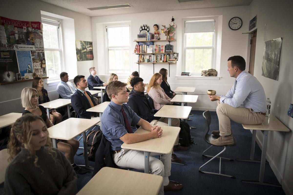 Teacher leading meditation session with boarding school students in peaceful classroom setting
