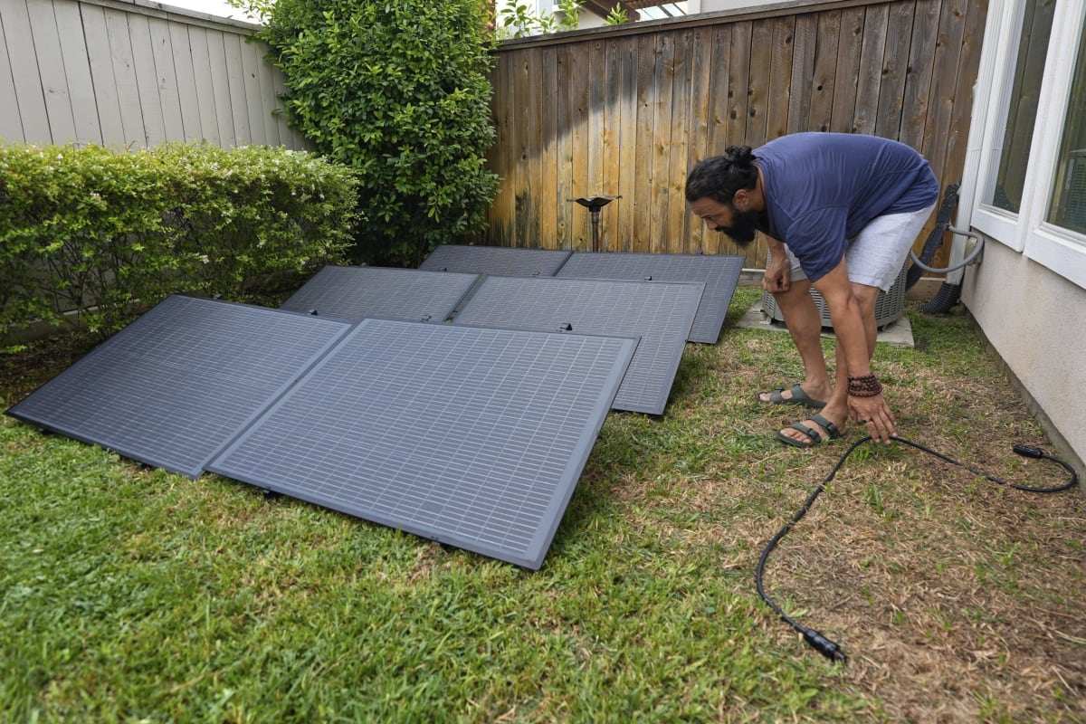 Compact solar panel mounted on apartment balcony railing beside outdoor plants and wall outlet