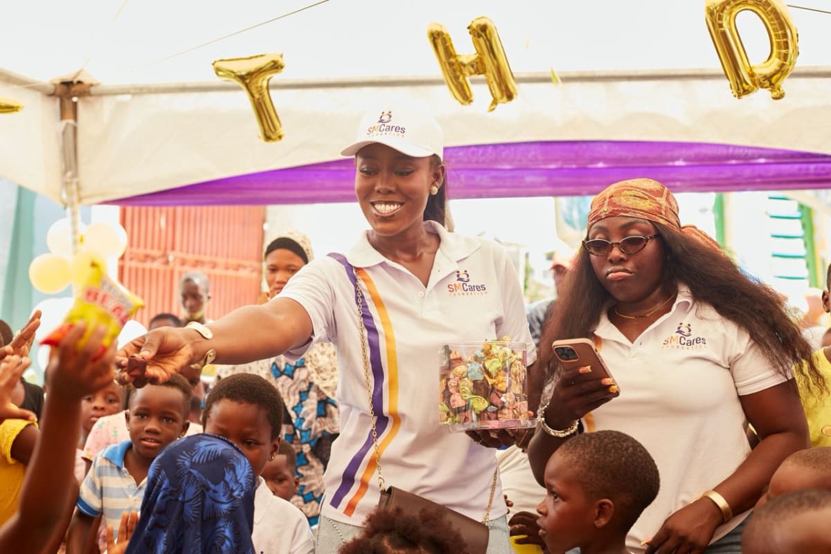 Sarah Mensah celebrating with smiling orphaned children receiving gifts in Ghana orphanage