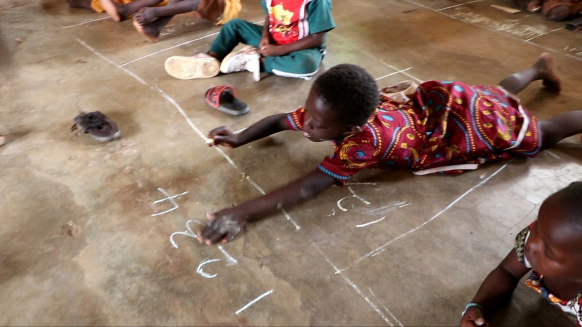 Ghanaian students sitting at new wooden desks in rural classroom after years learning on floor