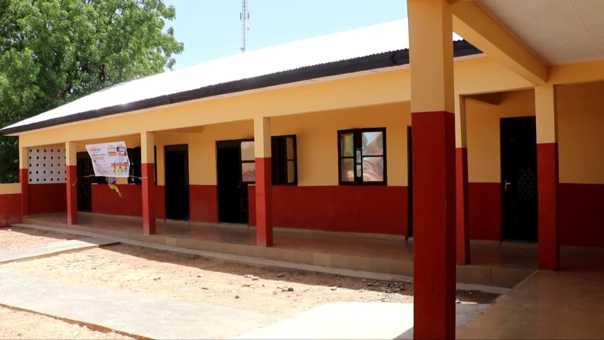 Modern school building in rural Ghana with children and teachers gathered outside for opening ceremony