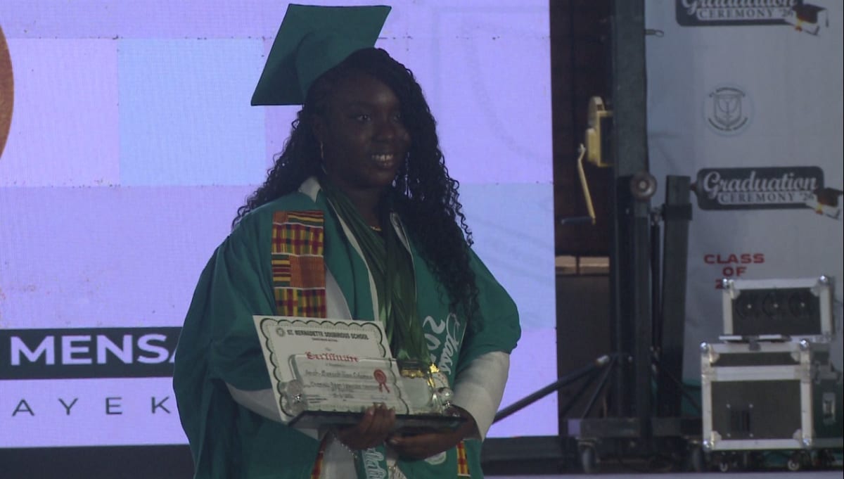 Young Ghanaian valedictorian in graduation gown delivering speech at school ceremony podium