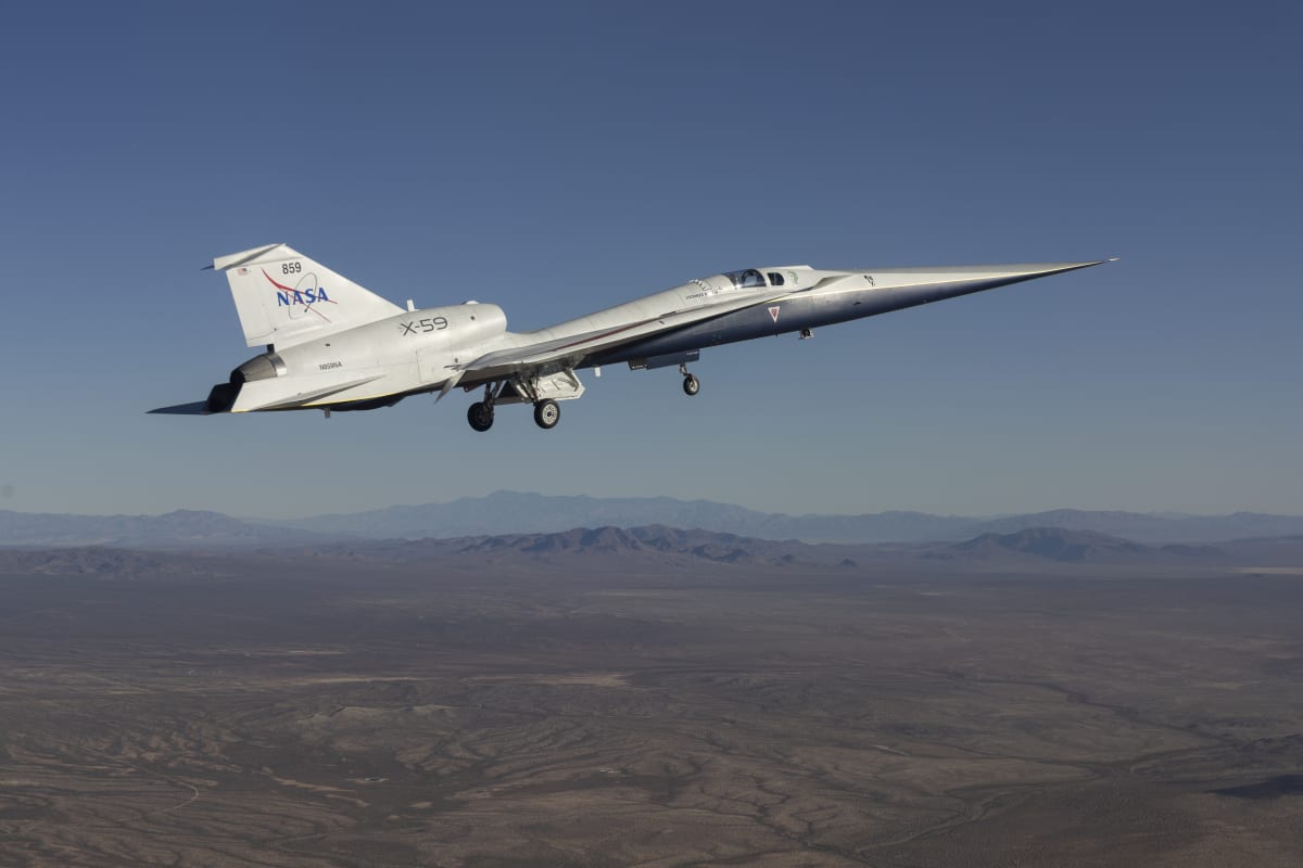 NASA's sleek silver X-59 experimental aircraft flying over California desert landscape during first test flight