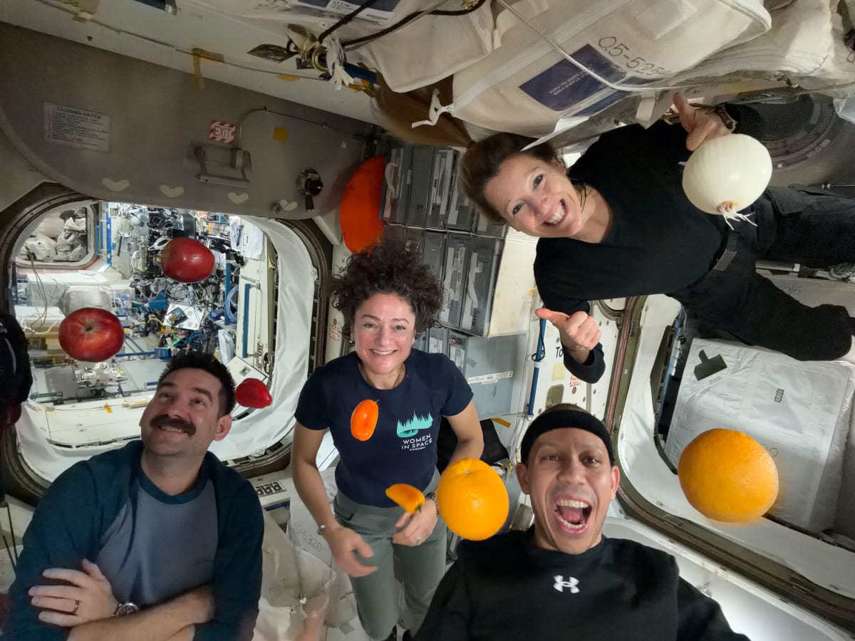 Four astronauts playfully toss fresh oranges and apples in zero gravity aboard space station