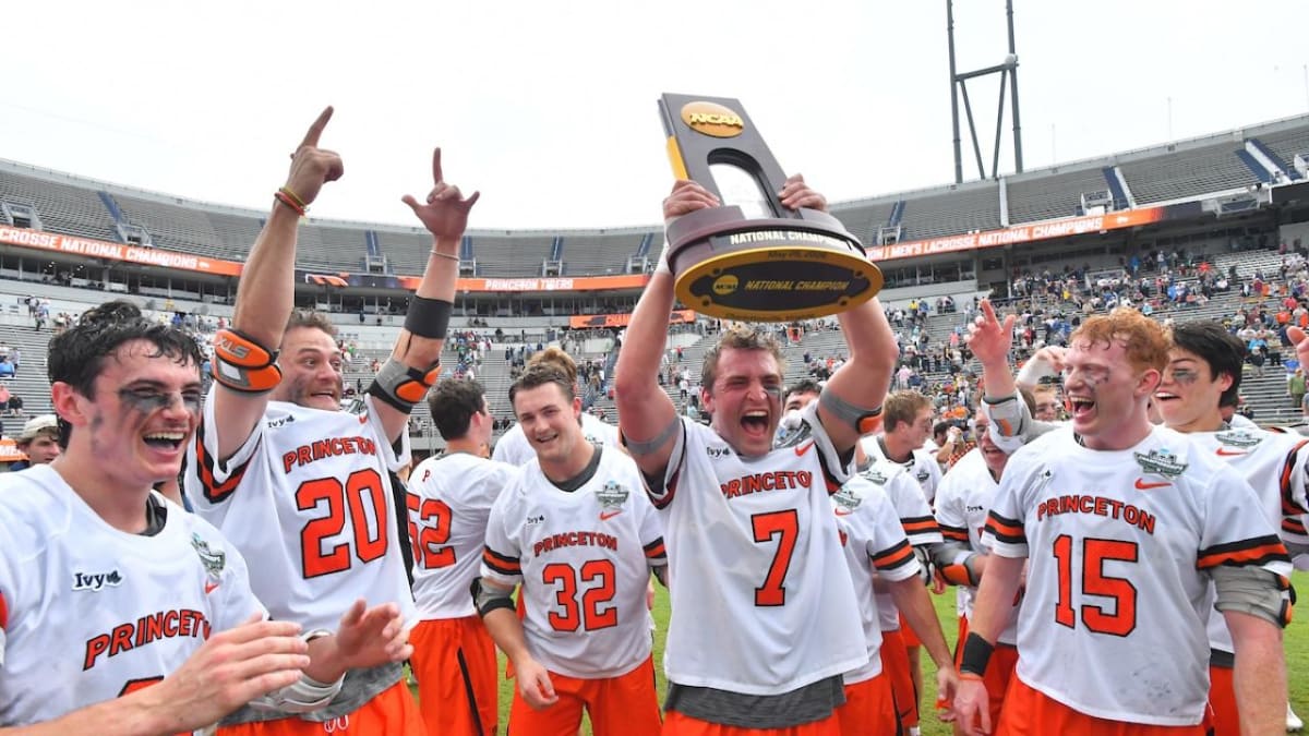 Princeton lacrosse players celebrating with championship trophy on field after defeating Notre Dame